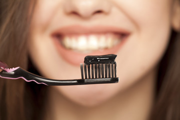 young woman holding a black tooth paste with active charcoal, and black tooth brush on white...