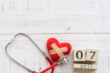 Wooden Block calendar for World health day, April 7. Healthcare and medical concept. Red heart with Stethoscope on Pastel white and blue wooden table background texture.