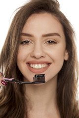young woman holding a black tooth paste with active charcoal, and black tooth brush on white...