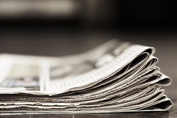 Pile of folded newspapers on wooden table for background. Daily papers with news (headlines, articles, photos) stacked in heap, side view with selective focus