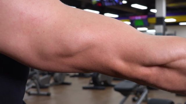 A fit man flexes his bicep in a gym - closeup