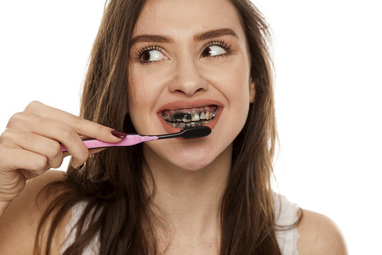 young woman brushing her teeth with a black tooth paste with active charcoal, and black tooth brush on white background, and showing thumbs up