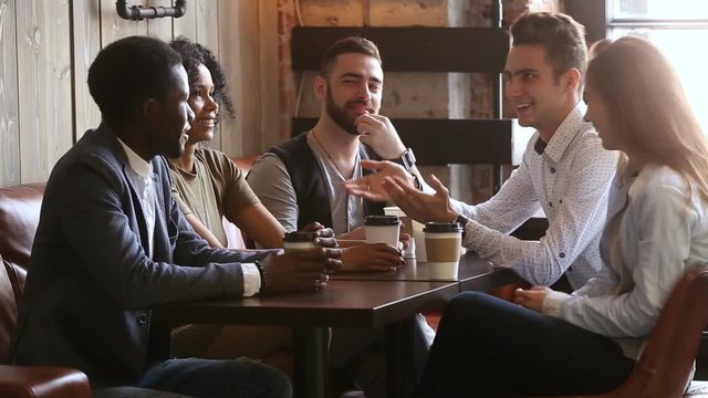 African and caucasian buddies making bet shaking hands at group meeting in coffeehouse, positive diverse young friends telling funny joke, laughing having fun while relaxing in cozy cafe with coffee