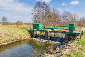 Fototapeta na wymiar Narrow bridge over a small river in a nature reserve in the Netherlands. There is a weir under the bridge. It is at the end of the winter season.