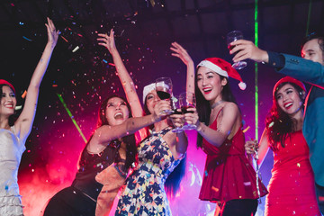 cheerful friends new year party in nightclub. Group of young people celebrate new year party throwing confetti and paper into the sky in night party at club. selective focus on woman in red hat.