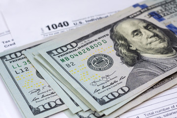 100 dollar bills on 1040 Individual Income Tax Return Form background, close up
