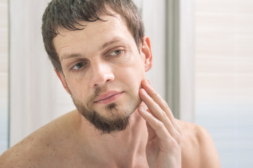 Naklejka premium The guy shaved one half of his face and looks in the mirror evaluating the result