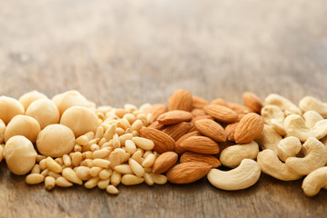 A bunch of almonds , macadamia nuts, pine nuts, cashews on an old brown wooden table, copy space