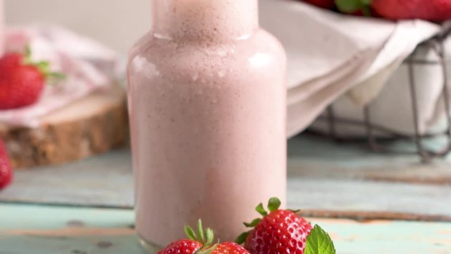 Healthy strawberry smoothie in a mason glass jar with scattered fruits over a rustic wood background