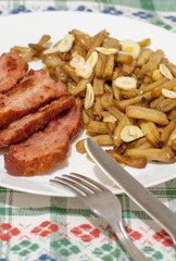 green beans with slices of fried bacon and decorated with slices of garlic on white plate on decorated tablecloth