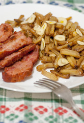 green beans with slices of fried bacon and decorated with slices of garlic on white plate on decorated tablecloth