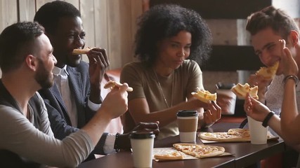 Multiracial happy young people eating pizza in pizzeria, black and white cheerful students enjoying meal dining sitting together at restaurant table, diverse hungry friends sharing lunch at meeting