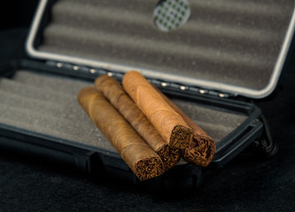 Cigars on top of a black travel humidor. Rich smelling and textures of tobacco leaves