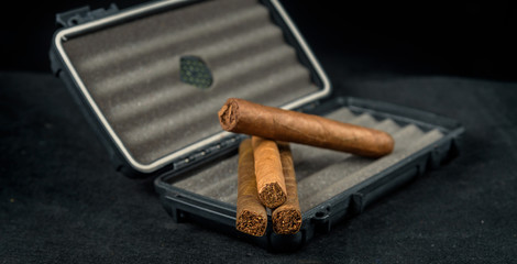 Cigars on top of a black travel humidor. Rich smelling and textures of tobacco leaves