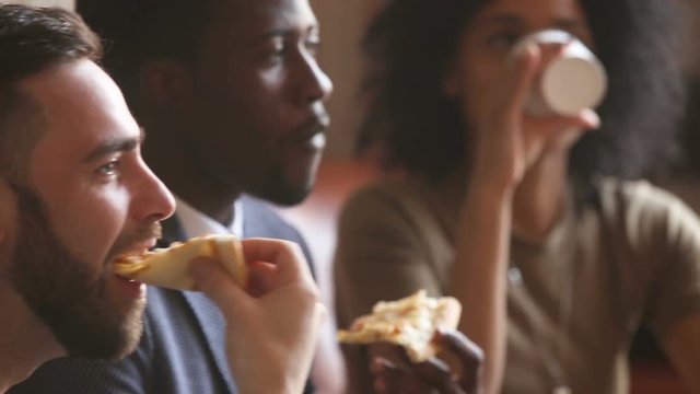 Multi-ethnic black and white friends eating pizza at meeting indoors, smiling happy diverse buddies enjoying italian food at home office, multiracial young people having lunch together in pizzeria