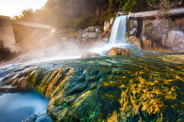 The stream of water in the waterfall flows and fall on stones with green moss and algae at dawn. Thermal springs Loutra Thermopilon, Greece.