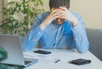 Sad man looking at his monthly bills at home.
