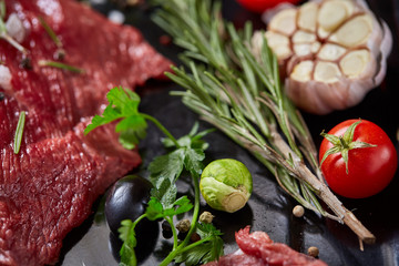 Flat lay of raw beefsteak with vegetables, herbs and spicies on metal tray, close-up, selective focus