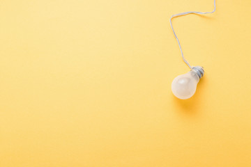 Light bulb on pastel yellow background top view, flat lay with copy space