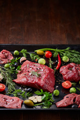 Flat lay of raw beefsteak with vegetables, herbs and spicies on metal tray, close-up, selective focus