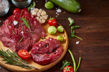 Flat lay of raw beefsteak with vegetables, herbs and spicies on metal tray, close-up, selective focus
