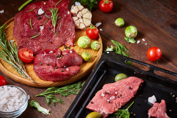 Flat lay of raw beefsteak with vegetables, herbs and spicies on metal tray, close-up, selective focus