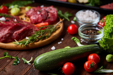 Flat lay of raw beefsteak with vegetables, herbs and spicies on metal tray, close-up, selective focus