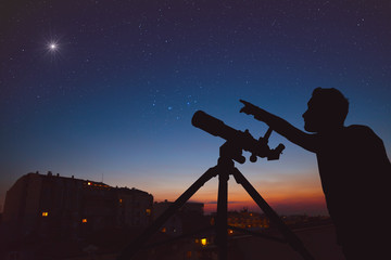 Young man looking at the sky with astronomical telescope in urban surroundings.