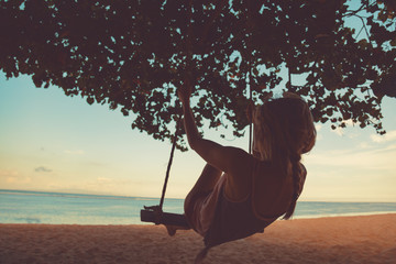 Young girl swinging on a sandy tropical beach.