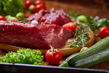 Still life of raw beef meat with vegetables on wooden plate over white background, top view, selective focus