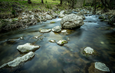 une rivière qui coule au milieu des prés avec des pierres et un rocher au milieu