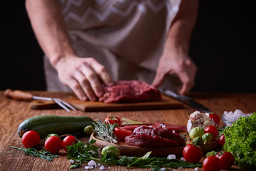 Strong professional man's hands cutting raw beefsteak, selective focus, close-up