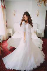 Fototapeta premium Beautiful bride posing in wedding dress in a white photo Studio. Mirror. Sofa. Bouquet. The door. Chandelier.