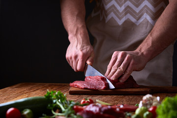Strong professional man's hands cutting raw beefsteak, selective focus, close-up