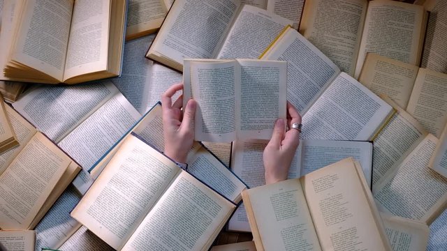 Woman flipping through the pages of a book and then reading. Close up of two hands with books covering woman and everything around her.