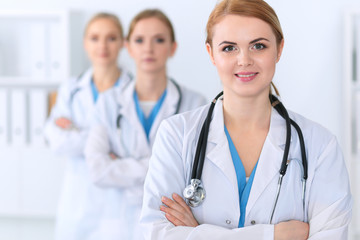 Beautiful female medical doctor standing at hospital in front of medical group. Physician is ready to help patients. Medicine and health care concept