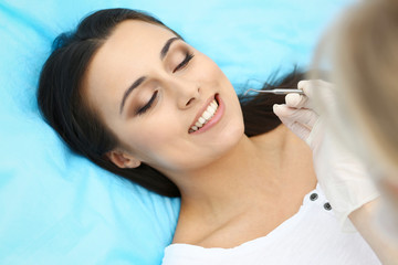 Young female patient visiting dentist office.Beautiful woman with healthy straight white teeth sitting at dental chair with open mouth during oral checkup while doctor working at teeth