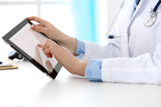 Closeup of a doctor sitting at the desk. Physician pointing into tablet pc. Medicine and health care concept