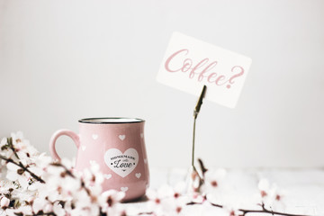 Pink coffee mug, white flowers and 'Coffee?' note, on white background
