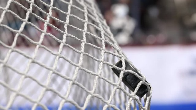 Hockey puck flies into the net on a hockey boards with a blue stripe. The movement at the beginning is accelerated then slowly
