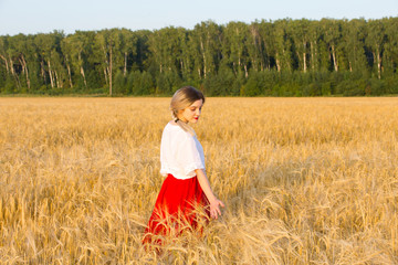 Naklejka na ściany i meble Lovely girl in a traditional costume walks on the field of cereals