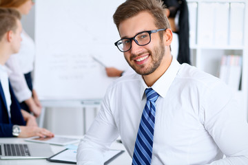 Business people at meeting in office. Focus at cheerful smiling bearded man wearing glasses. Conference, corporate training or brainstorming of people group. Success and negotiation concept