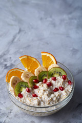 Delicious oatmeal porrige with fruits in glass bowl over white textured background, selective focus, flat lay, close-up.