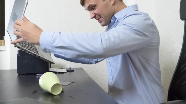 A young man poured tea onto a laptop. works in the office. Slow-motion shooting, 4k