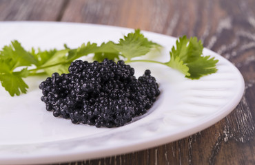 black caviar on a white plate with herbs on wooden