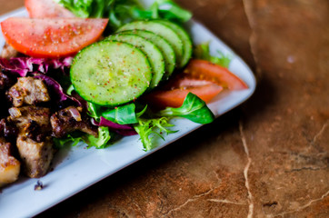 tasty dish with pork, lettuce, tomato and cucumber on a white plate with a dip