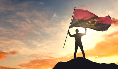 Angola flag being waved by a man celebrating success at the top of a mountain. 3D Rendering - obrazy, fototapety, plakaty