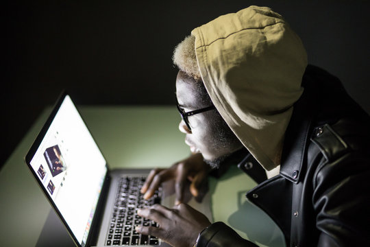 Handsome Afro American man using a laptop browse in internet till late at night. Afro man play games in darkness. Afro american hacker attack server in the night.