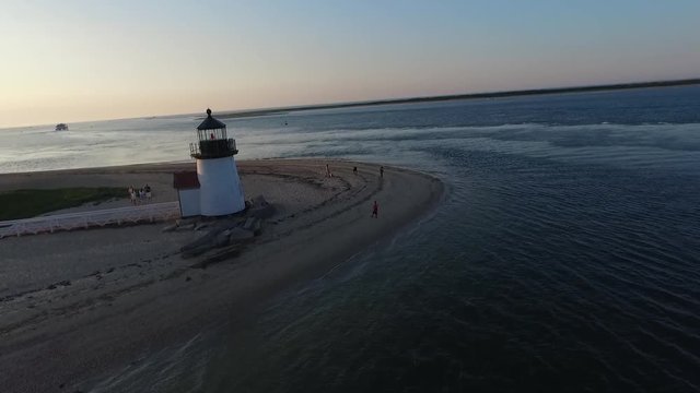 Drone passing lighthouse and beach goers at sunset