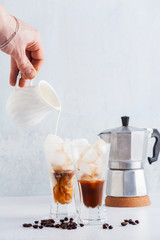 Man's hand pours milk on Iced coffee , beautiful and clean composition. coffee maker on back